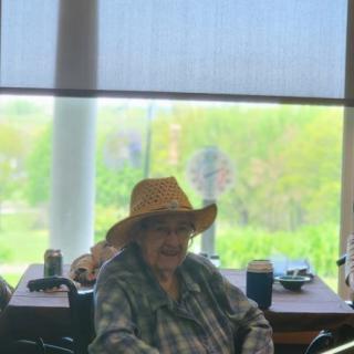A person wearing a hat sits indoors near a large window with natural light streaming in.