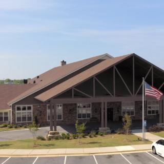 A large building with a prominent roof, an American flag, and a nearby parking lot under a clear sky.