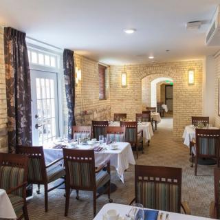 A cozy restaurant dining room with neatly arranged tables and chairs, featuring brick walls and natural light from large windows.