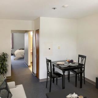 A cozy dining area in a modern apartment, featuring a table set for two and a view into the bedroom.