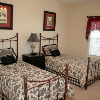 A cozy bedroom with twin beds, featuring patterned bedspreads, a lamp on a nightstand, and framed art on the walls.