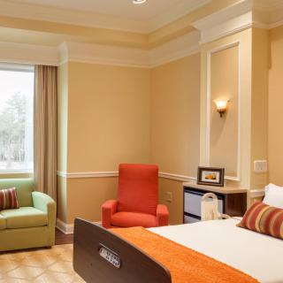 A cozy hotel room with a comfortable bed, armchair, and large window.