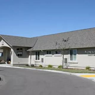 A medical clinic building with a pitched roof and a driveway in front, captured on a clear day.