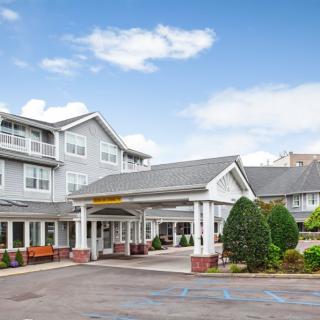 A hotel entrance with a neatly landscaped driveway under a blue sky with scattered clouds.