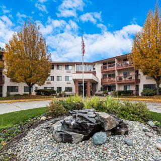 A multi-story residential building with autumn trees and a landscaped entrance under a partly cloudy sky.