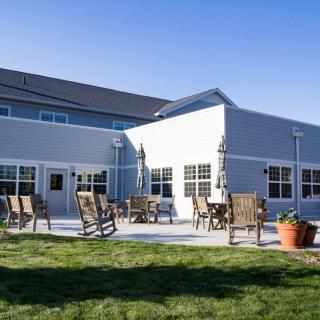 A sunny patio area with chairs and tables in front of a modern building.