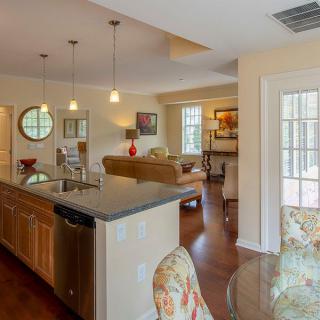 A modern open-concept living and kitchen area featuring wood flooring, pendant lighting, and a granite countertop.
