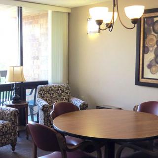 A cozy dining area with a round table and chairs, featuring a chandelier and artwork on the wall.