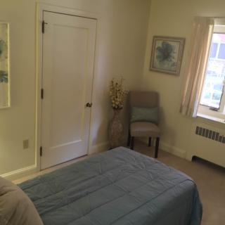 A neatly arranged bedroom with a bed, chair, and window.