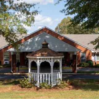 A picturesque gazebo in front of a brick building with surrounding landscaping.