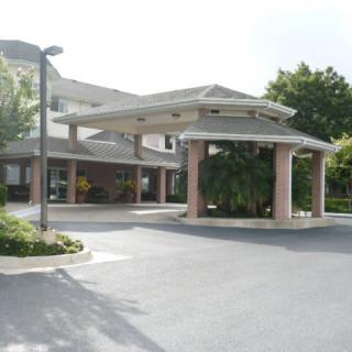 The image shows the entrance to a residential building with a covered driveway and surrounding greenery.