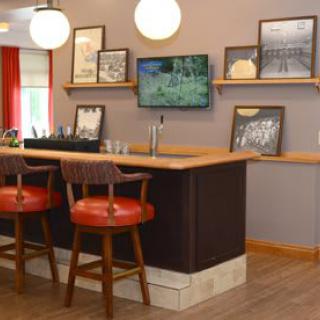 A cozy bar interior featuring a wooden counter, red cushioned chairs, framed pictures on the walls, and a small television.