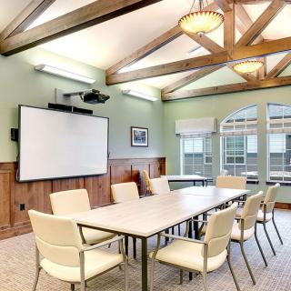 A well-lit conference room featuring a large table, several chairs, a projector, and a whiteboard.