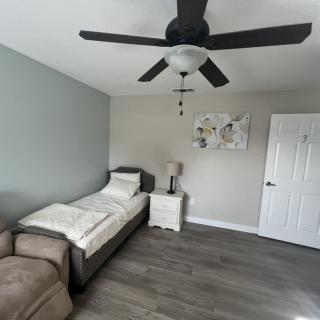 A minimalist bedroom featuring a single bed with white bedding, a ceiling fan, and modern decor.