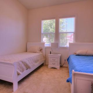 A cozy bedroom with two twin beds, a nightstand, and large windows.