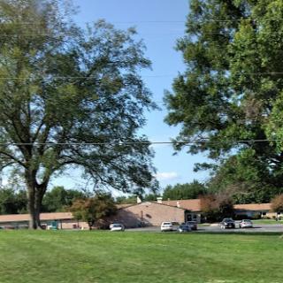 A peaceful view of a building surrounded by trees and green grass under a clear blue sky.