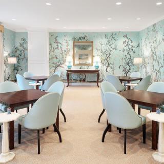 An elegant dining room with pastel-colored chairs and tables, featuring floral wallpaper and soft lighting.