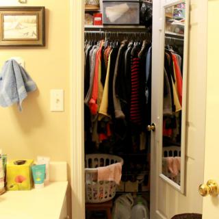 A bathroom with an open closet full of hanging clothes and a laundry basket.