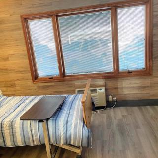 A simple room with wooden walls featuring a hospital bed by a large window with blinds.