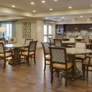A spacious and elegantly designed dining area with multiple tables and chairs, featuring warm lighting and a wooden floor.