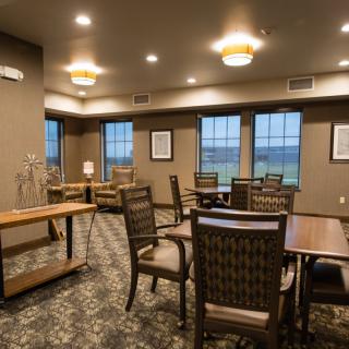 A cozy dining room with multiple tables and chairs, warm lighting, and large windows.
