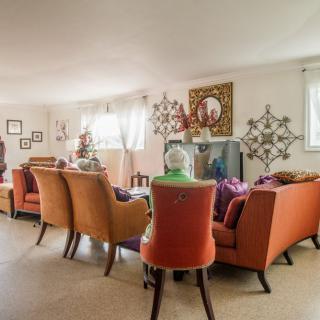 A cozy living room with orange and red chairs arranged around a television, featuring decorative elements on the walls.