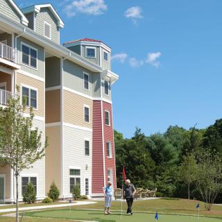 A couple of people standing on the lawn near a multi-story apartment building with trees in the background.