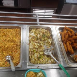 A variety of dishes available in a cafeteria setting, including rice, mixed vegetables, and fried snacks.