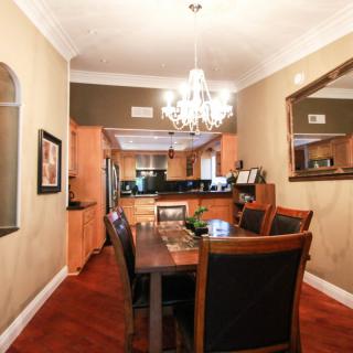 A cozy dining room with wooden furniture and a chandelier, opening into a modern kitchen.