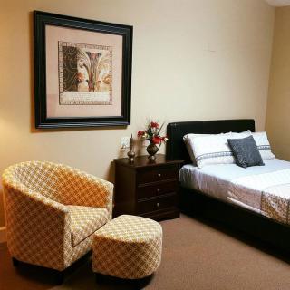 A cozy bedroom with a bed, an upholstered chair, and a framed artwork on the wall.