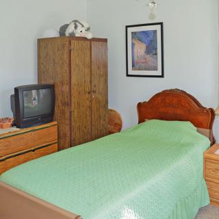 A small bedroom with a single bed, wooden furniture, and an old-style television.