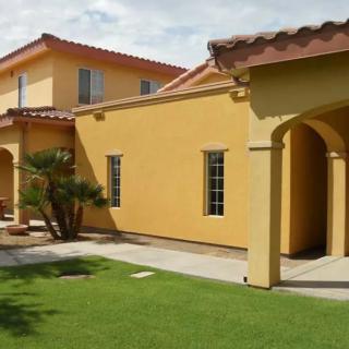 A Spanish-style house with orange stucco walls and a red-tiled roof, surrounded by a well-maintained lawn.