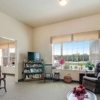 A cozy living room with a television, comfortable seating, and large windows letting in natural light.