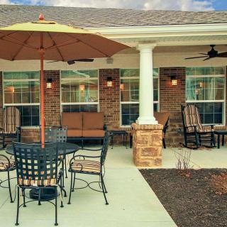 A cozy outdoor patio featuring seating with a large umbrella, adjacent to a brick house.