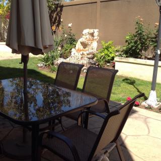 A sunny patio with a glass table, chairs, and garden view.