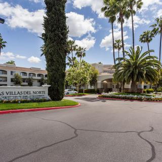 Entrance to an apartment complex with palm trees and a well-maintained landscape.