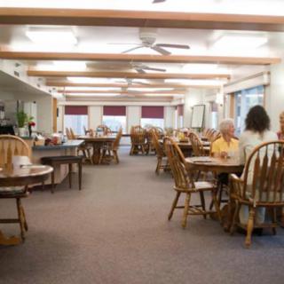 A cozy dining area with wooden tables and chairs, occupied by a few people having a meal.