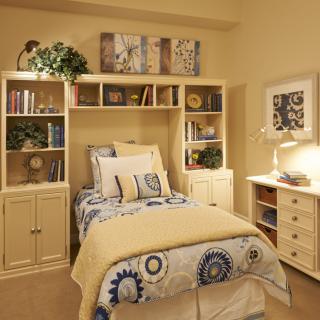 A cozy bedroom with a neatly made bed, surrounded by bookshelves and warm lighting.