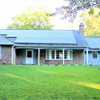 A suburban house with solar panels on the roof and a well-maintained front lawn.
