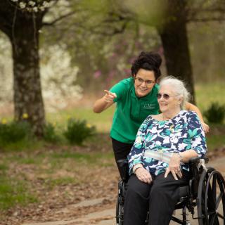 A caregiver and an elderly woman in a wheelchair enjoying a day at the park.