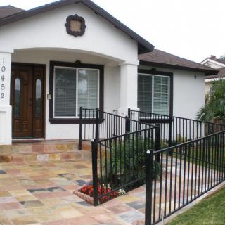 A small house with a front entrance featuring a ramp and fenced pathway.