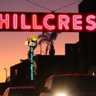 A neon sign reading 'Hillcrest' illuminates the street at sunset.