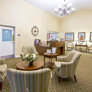 A cozy lobby area featuring striped chairs around a small round table with flowers, a reception desk in the background, and wall decor including clocks and framed pictures.