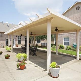 A spacious outdoor patio area with a pergola, featuring tables and chairs, surrounded by potted plants.