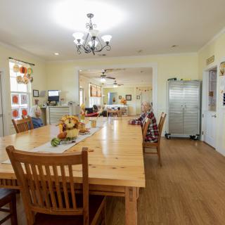 Spacious dining room with a large wooden table and chairs, decorated with a chandelier and various home decorations.