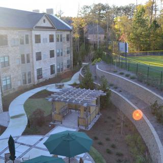 A sunlit view of an apartment complex with landscaped walkways and a gazebo.