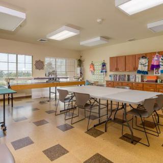 An art classroom with tables and chairs, featuring large windows and cabinets.