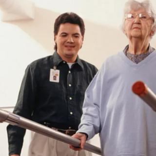 A caregiver assists an elderly person during physical therapy.