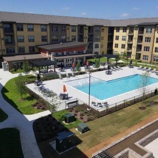 Aerial view of an apartment complex featuring a central swimming pool and landscaped outdoor area on a sunny day.