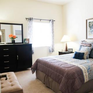 A cozy bedroom with a neatly made bed, dresser, and soft lighting.